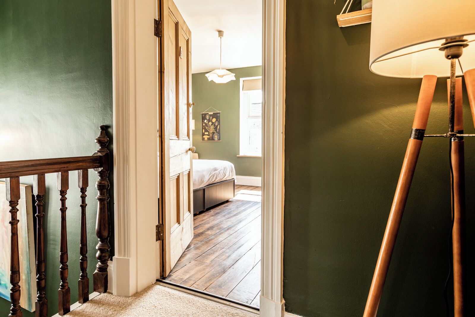 Um corredor que leva a um quarto com assoalho de madeira, uma cama e um lustre.