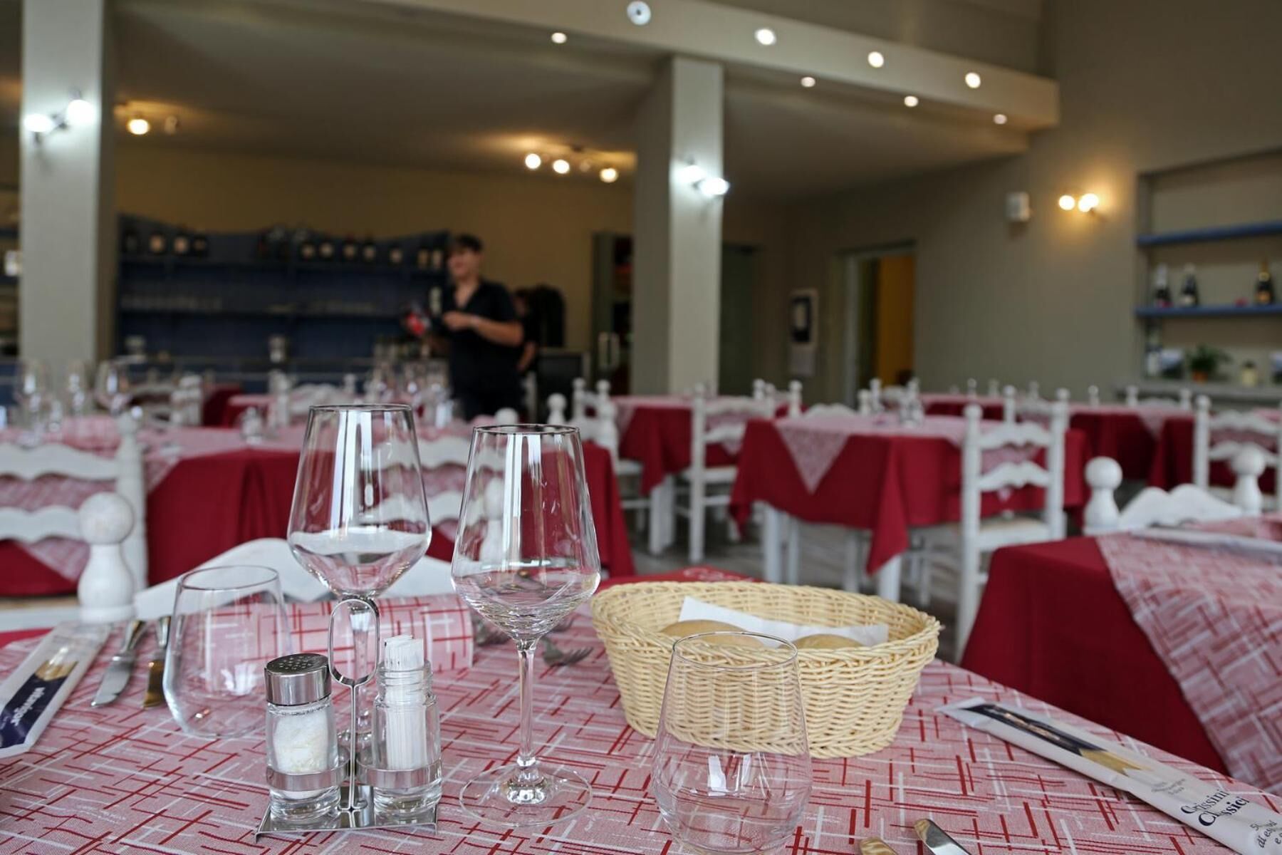 Een restaurant met gedekte tafels, helder glaswerk en een broodmand.