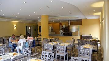 Un restaurante con varias mesas y sillas, una zona de bar y una cocina al fondo.