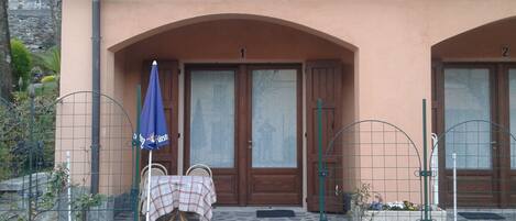 A building with two arched doorways, a table with a checkered tablecloth, and a blue umbrella.