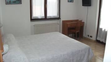Un dormitorio con cama, escritorio, silla, radiador y televisor en la pared.