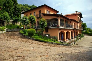Uma casa de dois andares com um caminho de paralelepípedos, rodeada por vegetação e um muro de pedra.