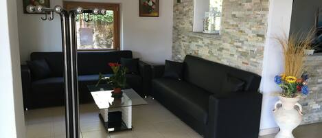 A modern living room with a black sofa, a glass coffee table, and a white vase with flowers.