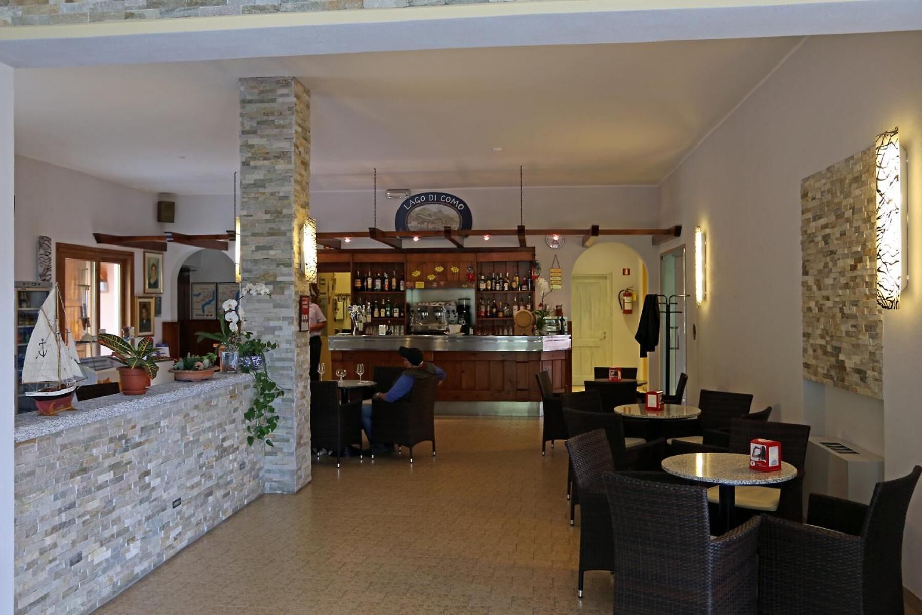 A bar area with a stone pillar, wooden ceiling beams, and a bar counter. There are tables and chairs for seating.