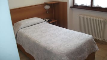 Een enkel bed met een beddekleed met patroon in een kamer met een houten hoofdeinde, een nachtkastje met een lamp en een raam met uitzicht.