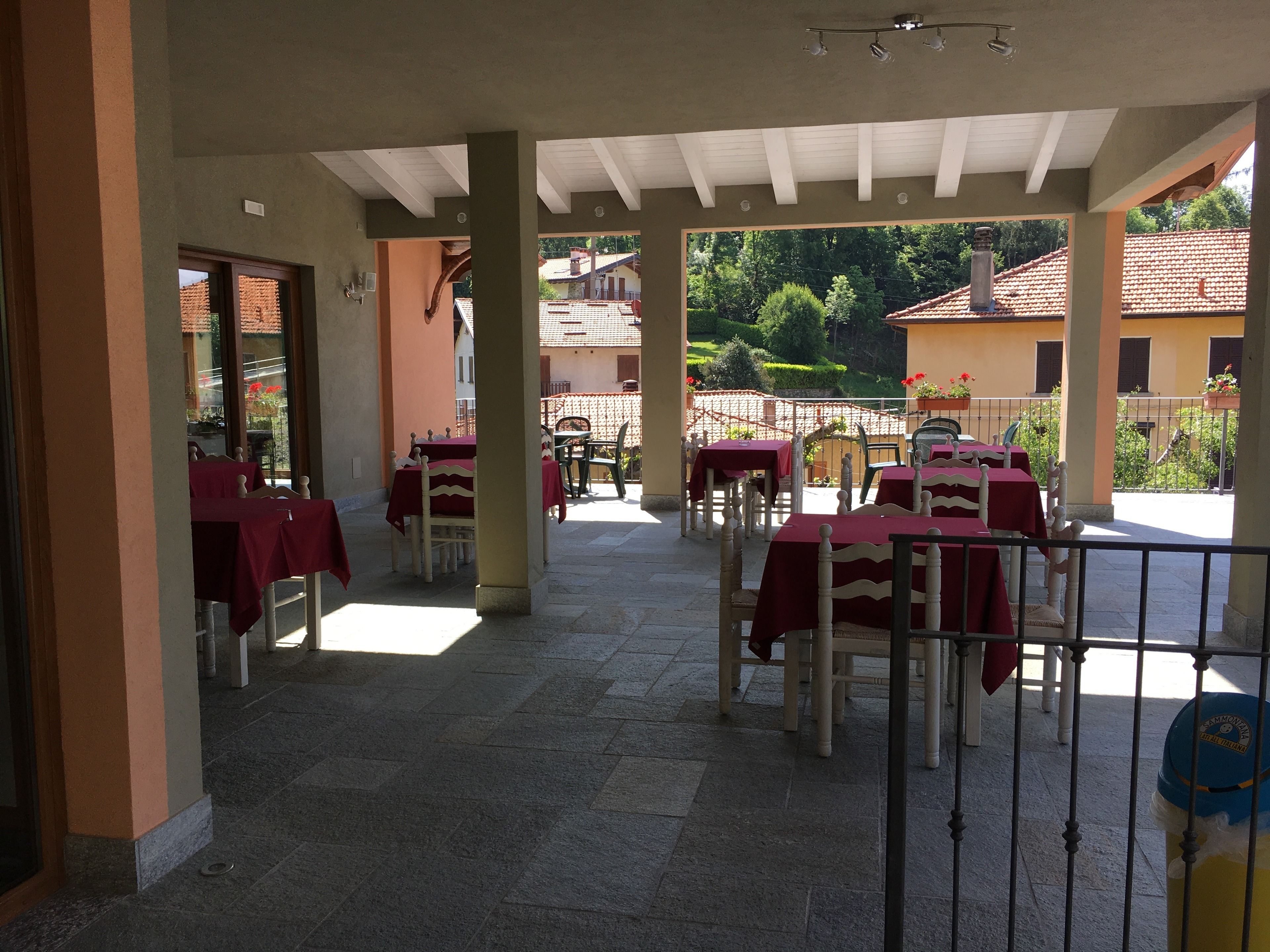 Zona patio esterna con tavoli e sedie, coperta da un tetto con travi bianche.