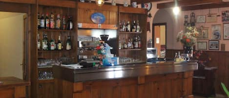 Un espace bar avec des étagères en bois remplies de bouteilles et de verres, un appareil à café et une enseigne indiquant « FORETTI ».
