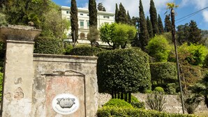 A historic building with a stone entrance, surrounded by lush greenery and tall trees. - Villa Alta (San Giuliano Terme)