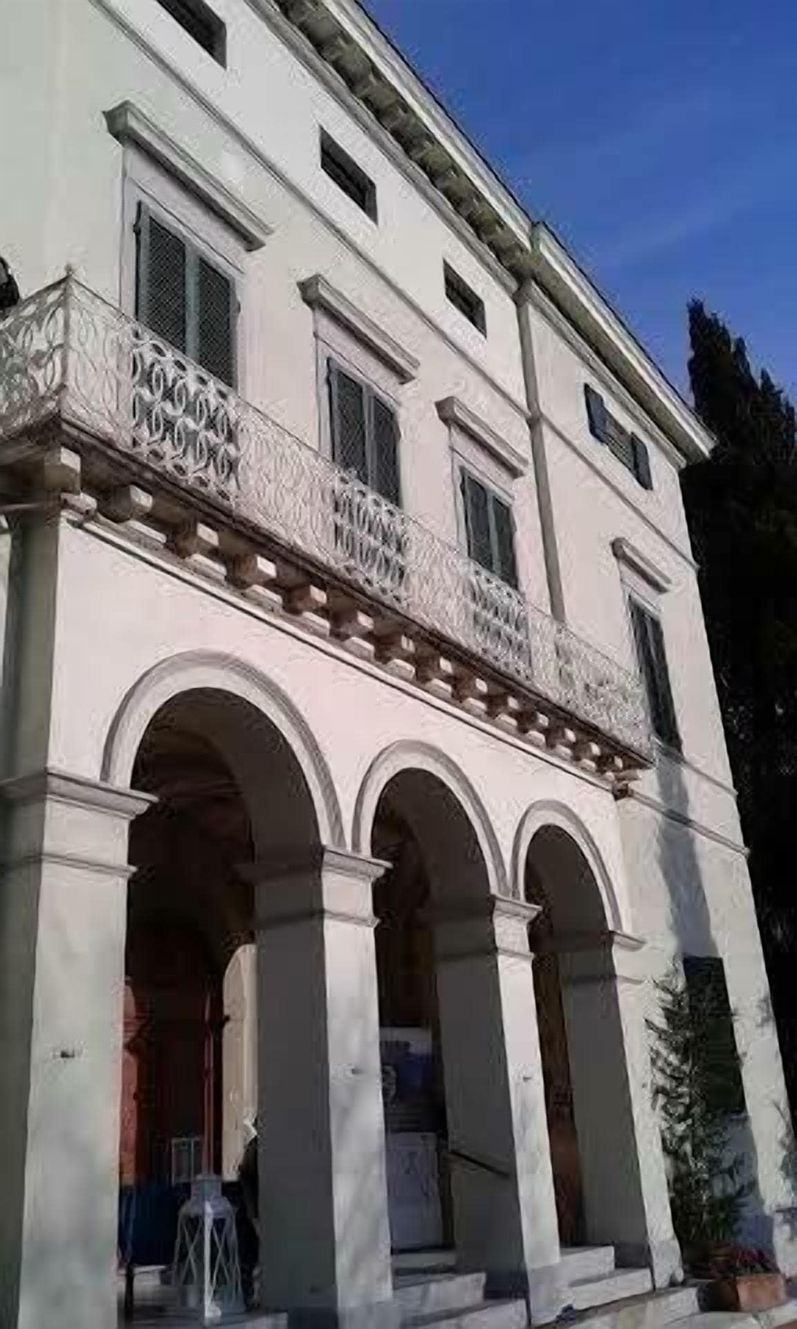 A building with a classical architectural style, featuring a balcony with ornate balustrades and a series of arches supporting the structure.