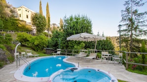 A swimming pool with two hot tubs, lounge chairs, and an umbrella. - Villa Alta (San Giuliano Terme)