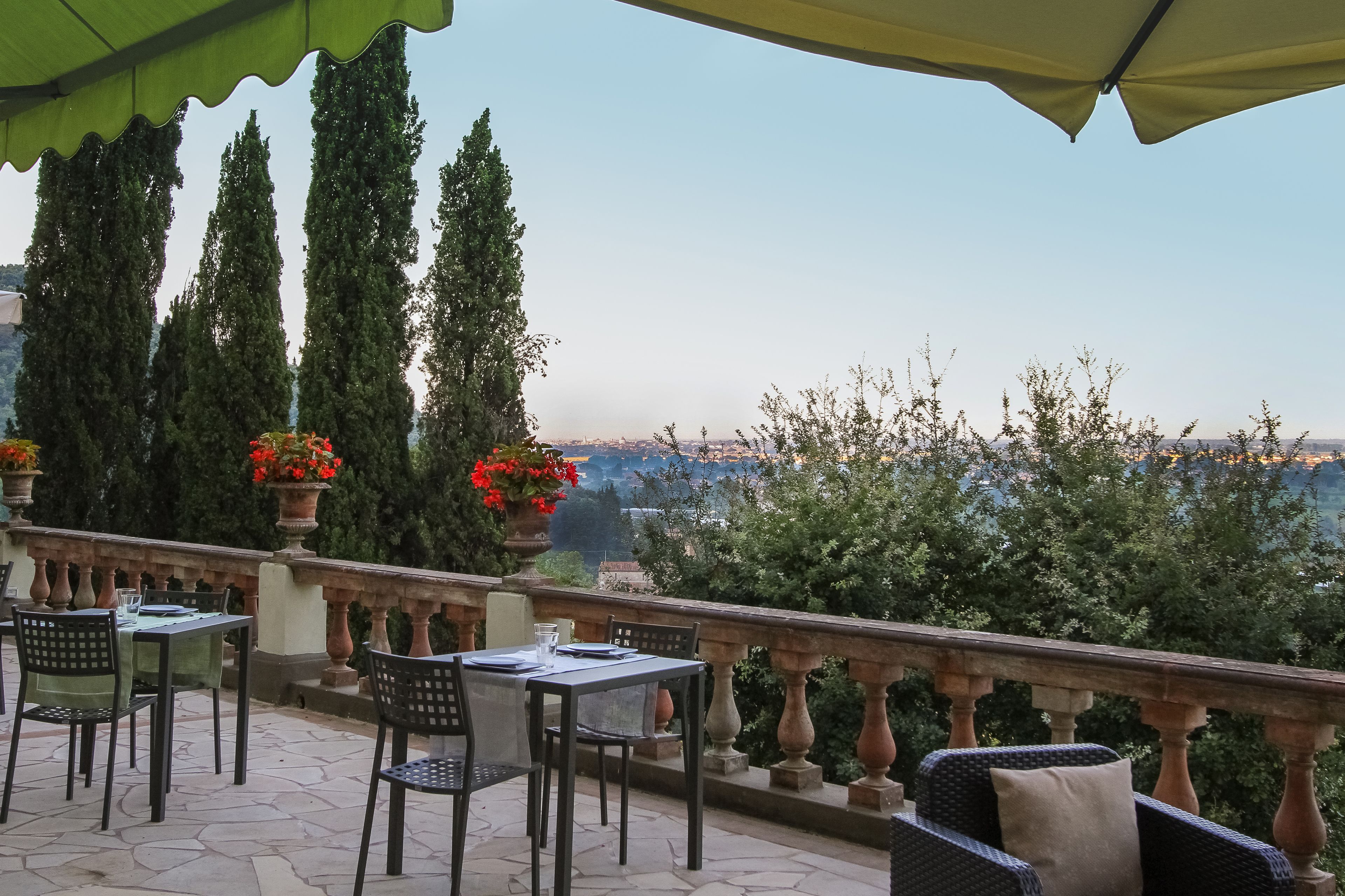 A terrace with outdoor seating, a view of the city, and tall trees.