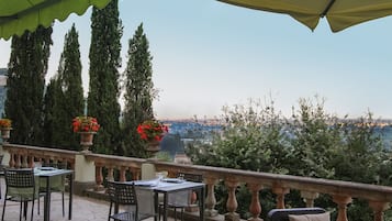 A terrace with outdoor seating, a view of the city, and tall trees.