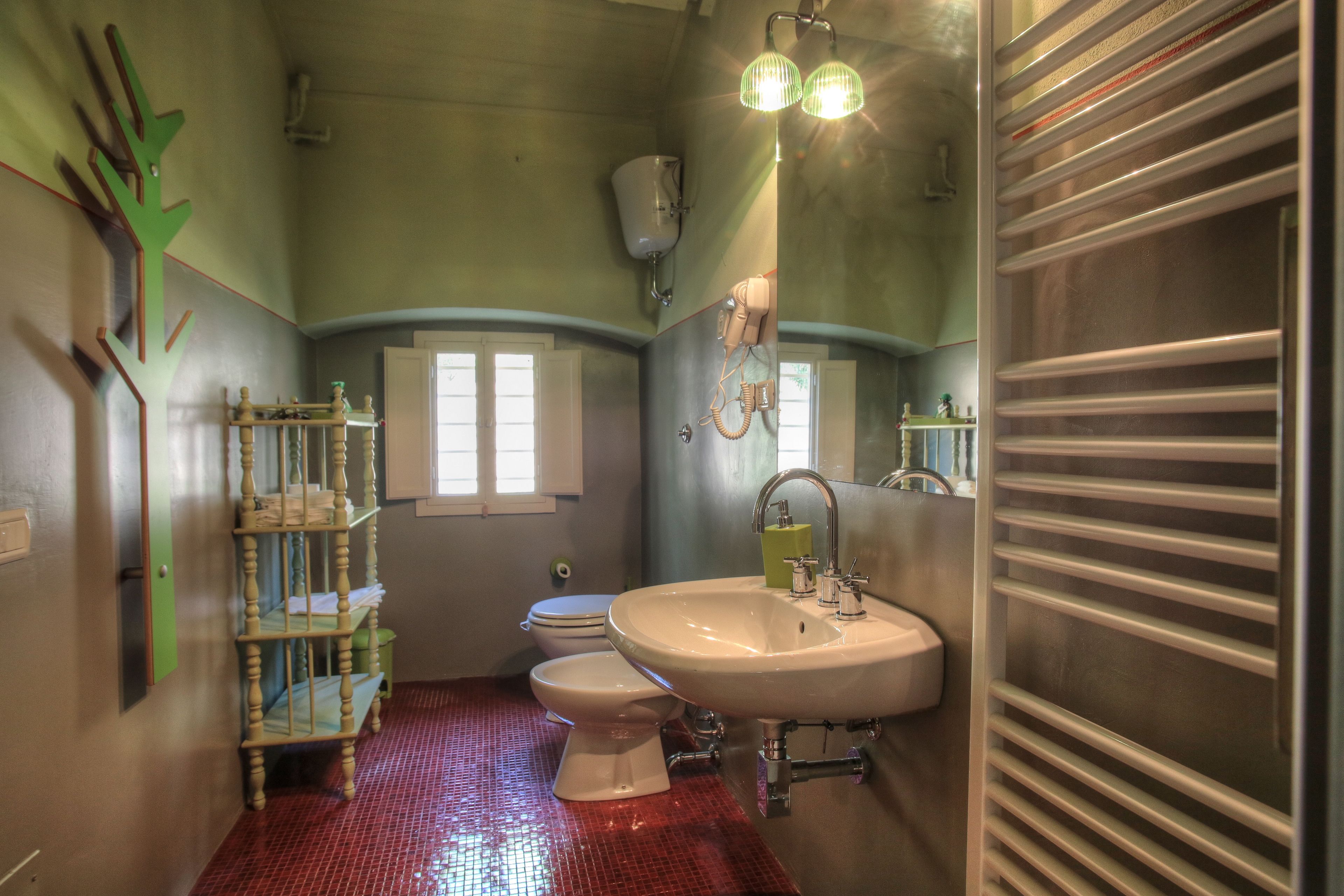 Une salle de bain avec un sol carrelé de carreaux rouges, un lavabo blanc, des toilettes et une étagère verte.