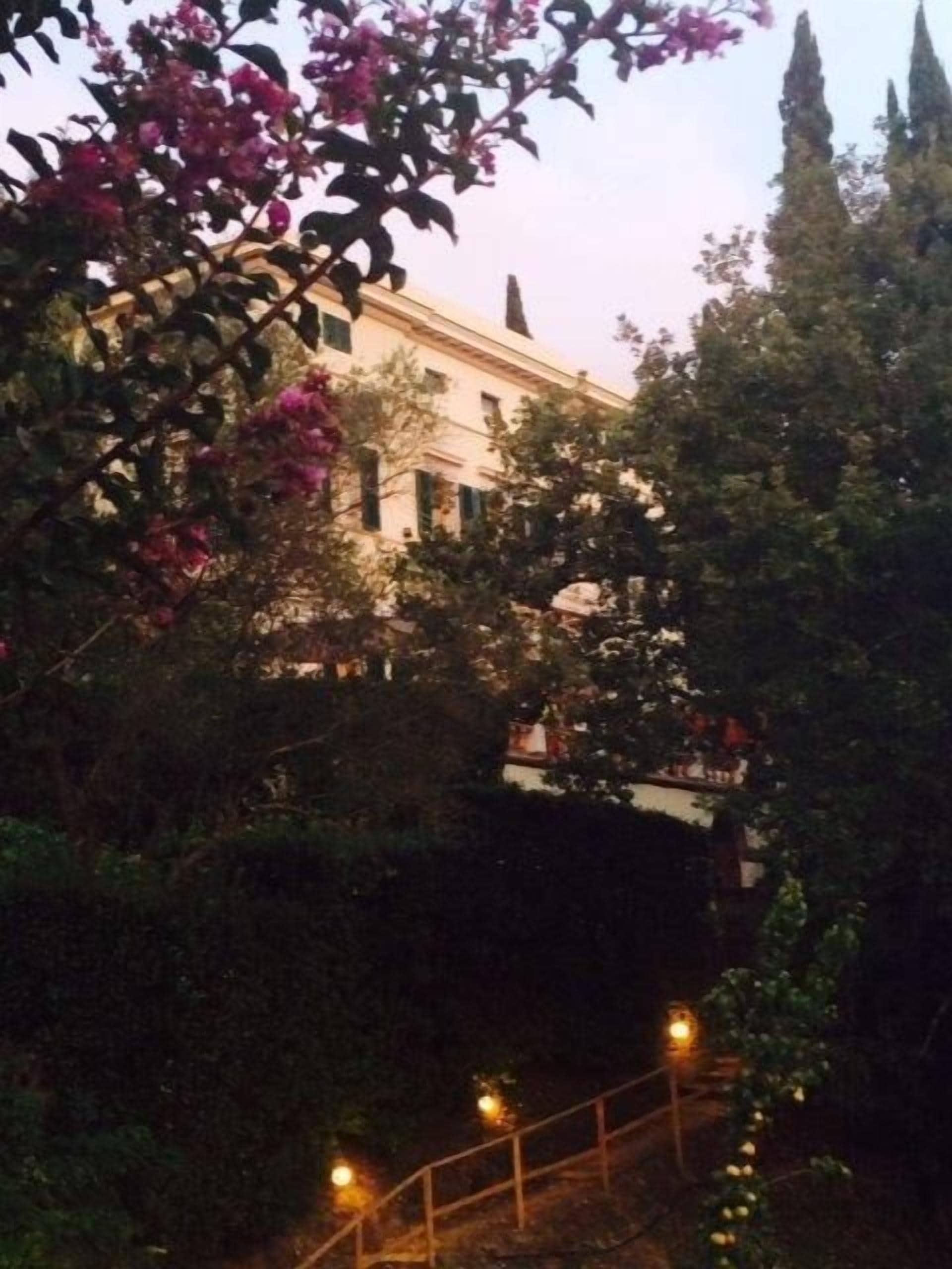 A building with a classical architectural style, surrounded by lush greenery and flowering plants.