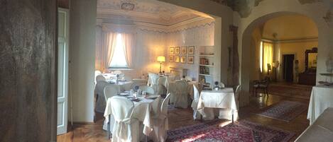 A dining area with tables set for a meal, a chandelier, and a fireplace.
