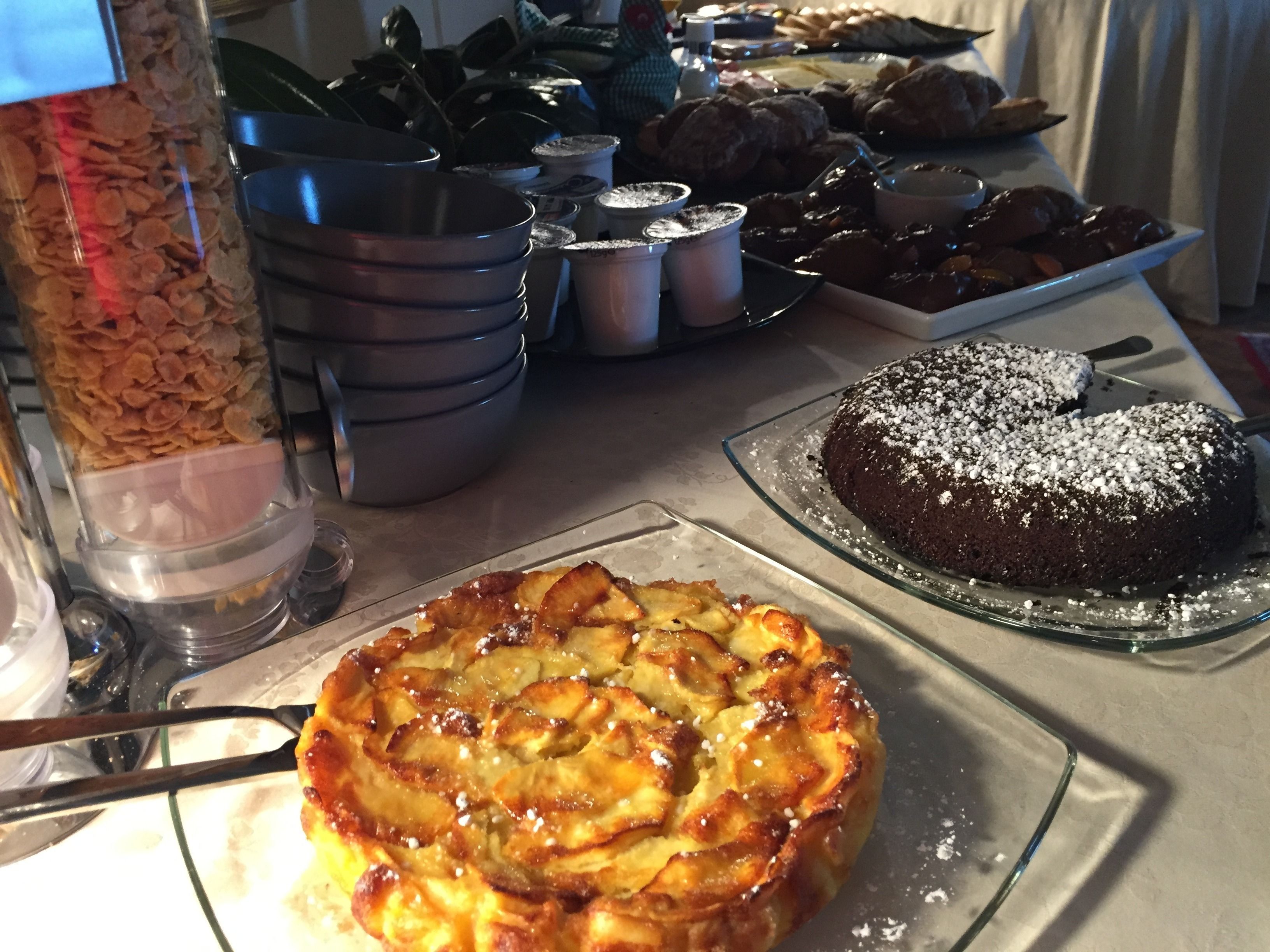 A buffet table with various dishes including a cake, a fruit tart, and a container of cereal.