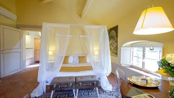 A bedroom with a four-poster bed, a bedside table with a tray of breakfast items, and a large window with a view of the outside.