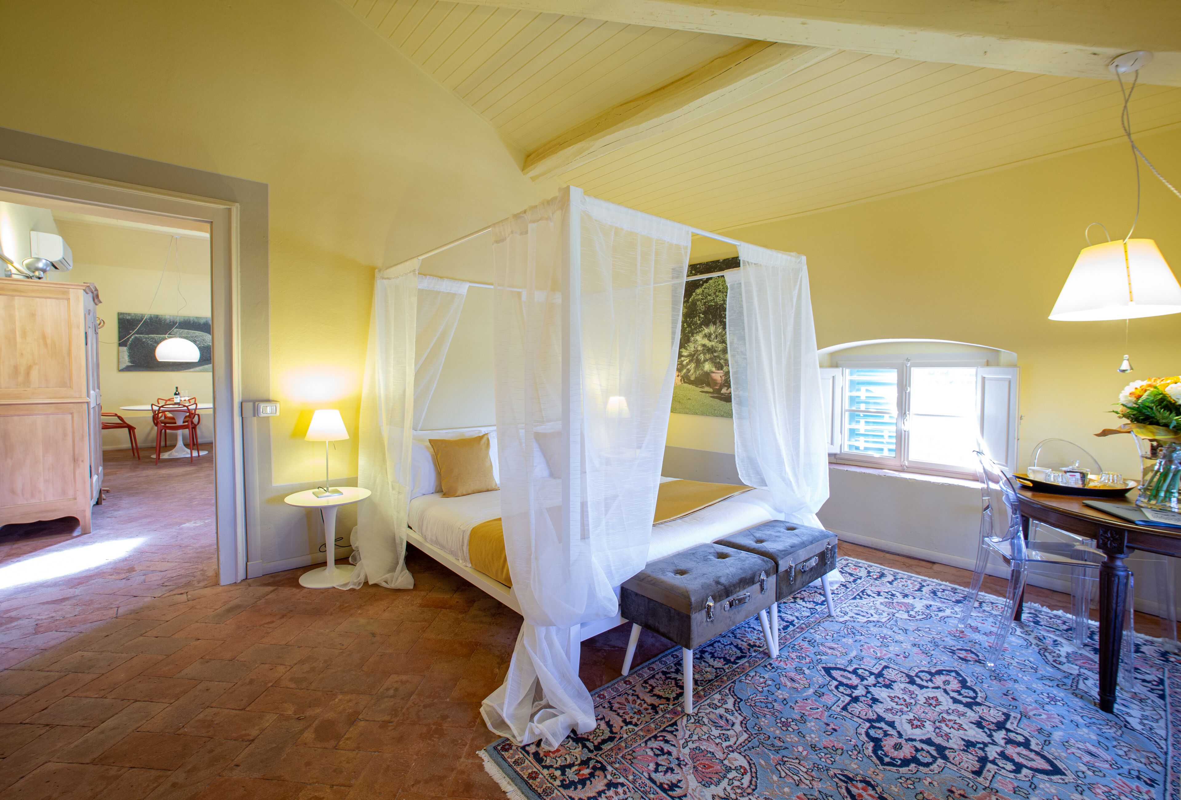 A bedroom with a four-poster bed, a small table with a lamp, and a chair.