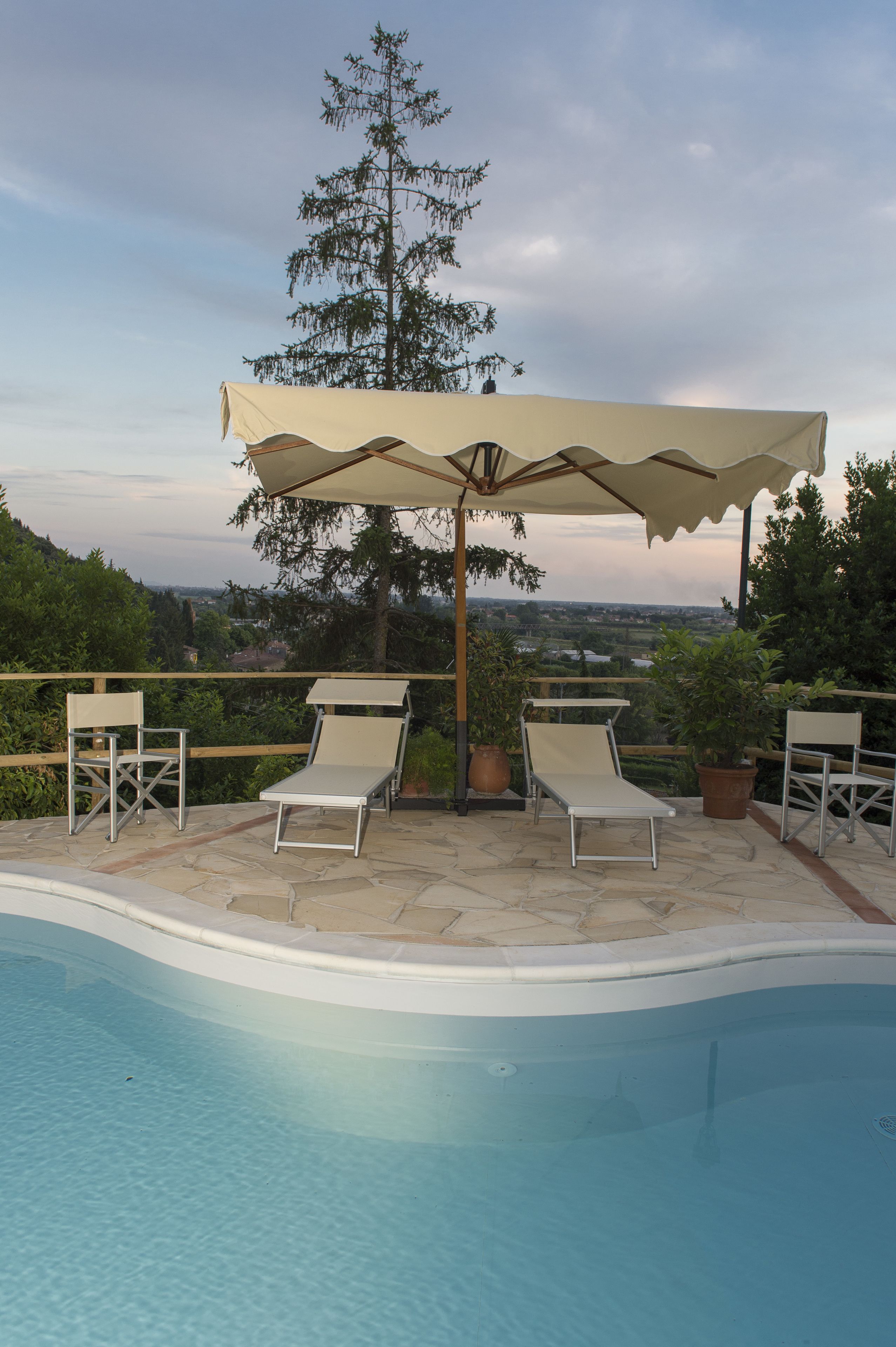 Una piscina con lettini e ombrellone, circondata da piante in vaso e vista sul paesaggio.