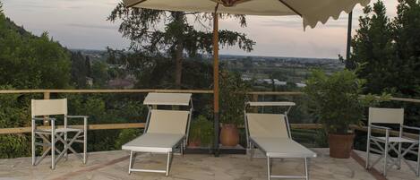 Una piscina con sillones de descanso y una sombrilla, rodeada de plantas en macetas y vistas al paisaje.