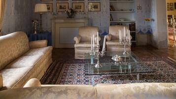 A room with a patterned wall, a sofa, a chair, a glass coffee table, and a fireplace.