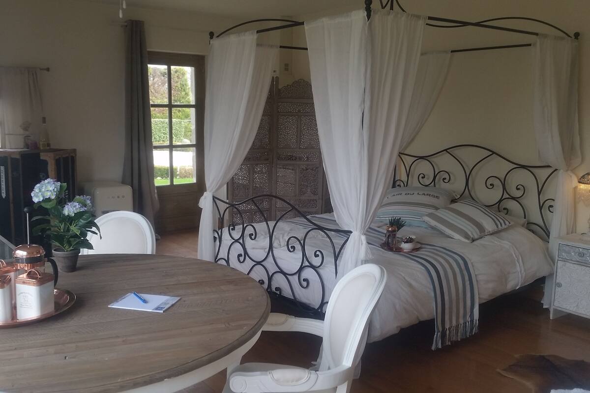 A bedroom with a four-poster bed, a round wooden table with coffee cups, and a chair.