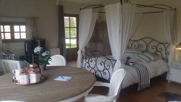 A bedroom with a four-poster bed, a round wooden table with coffee cups, and a chair.