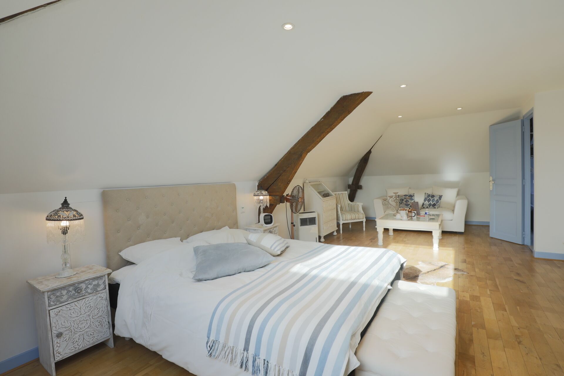 Une chambre à coucher avec un grand lit, une table de chevet, une chaise, une petite table et un ventilateur de plafond.