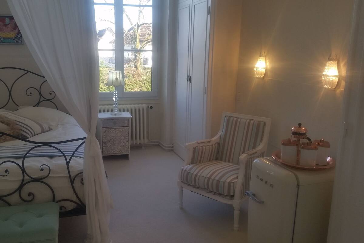 A bedroom with a bed, a chair, a small table, and a radiator.
