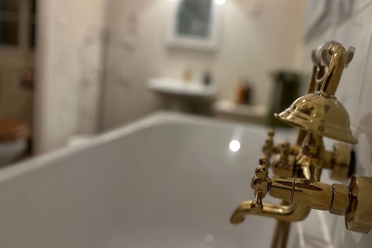 A bathtub with gold fixtures, a white sink, and a mirror in a bathroom.