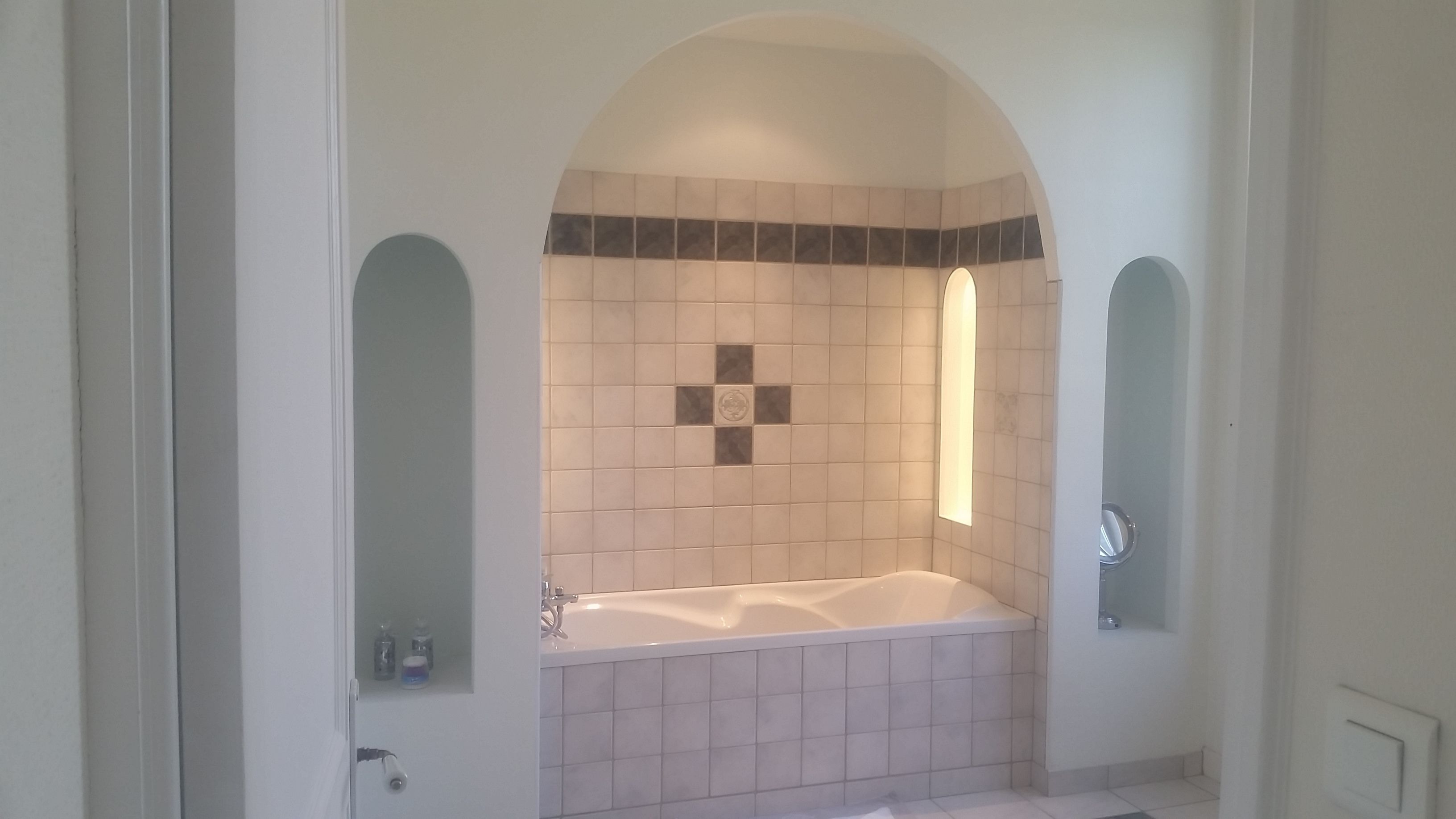 A bathroom with a freestanding bathtub, a tiled wall with a decorative pattern, and a mirror on the wall.