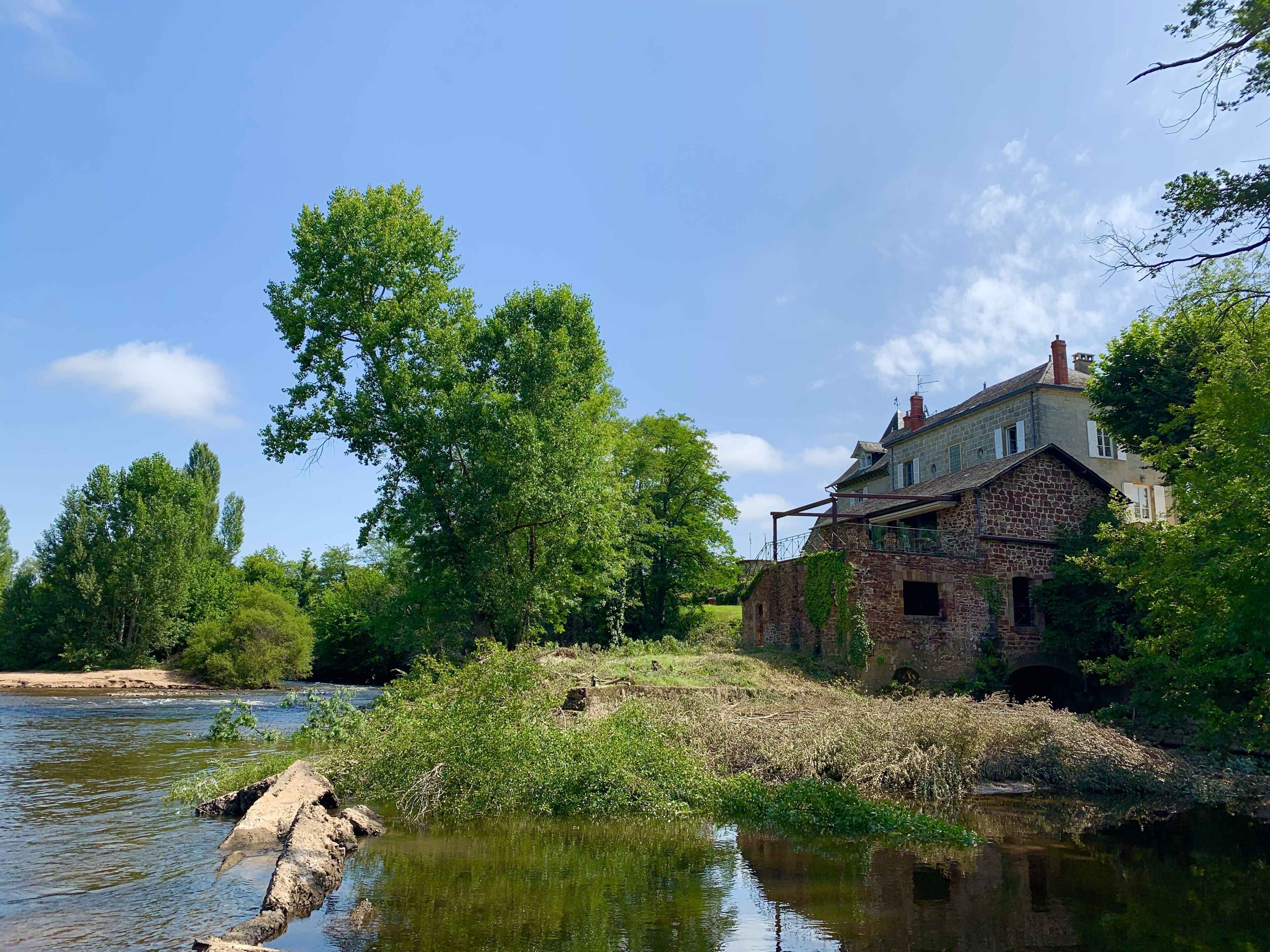 A stone building with a stone bridge over a river, surrounded by trees and greenery.