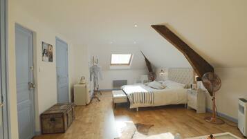 A bedroom with a sloped ceiling, a bed, a radiator, a fan, a dresser, a suitcase, and a cowhide rug.