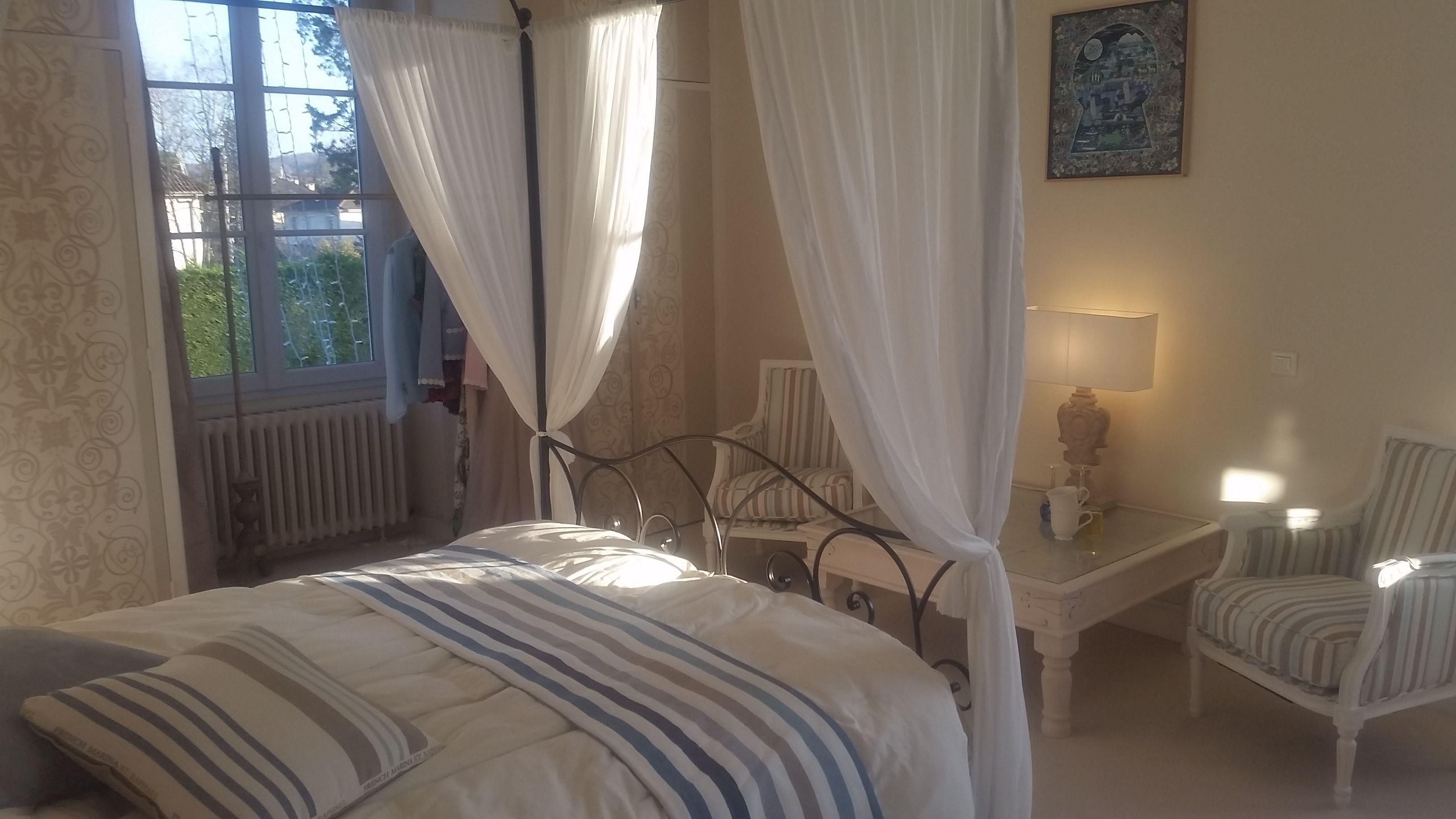 A bedroom with a bed, a chair, a table with a lamp, and a window with curtains.