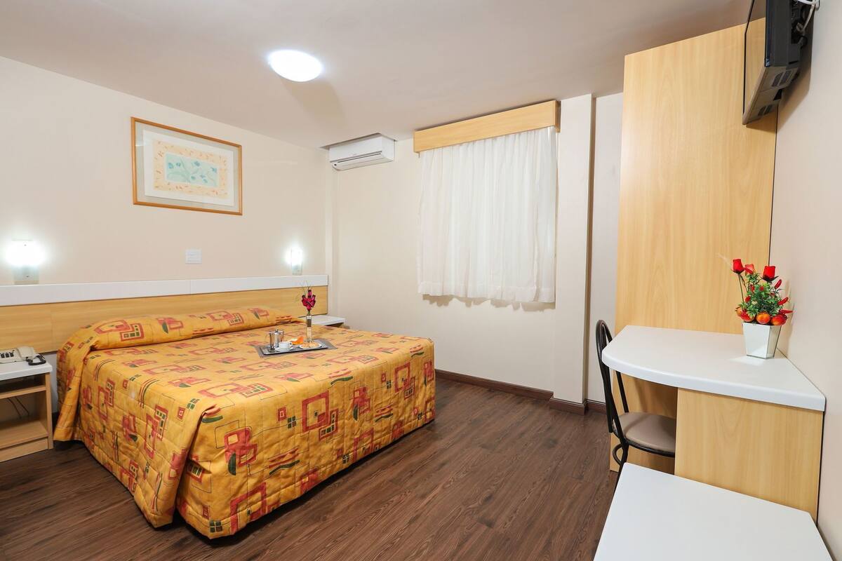 Ein Hotelzimmer mit Bett, Nachttisch, Schreibtisch, Stuhl und Fernseher.