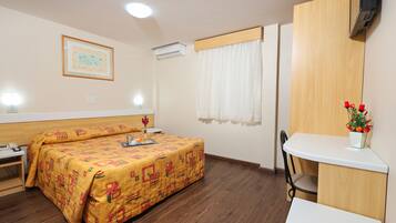 A hotel room with a bed, a desk, a chair, a TV, and a window with curtains.