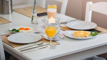 A breakfast table set with plates, cutlery, a candle, and a glass of orange juice.
