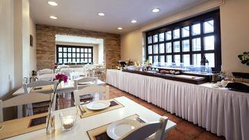 Ein Essbereich mit weißen Tischen und Stühlen, eine Buffettheke mit verschiedenen Speisen und ein großes Fenster, das für natürliches Licht sorgt.
