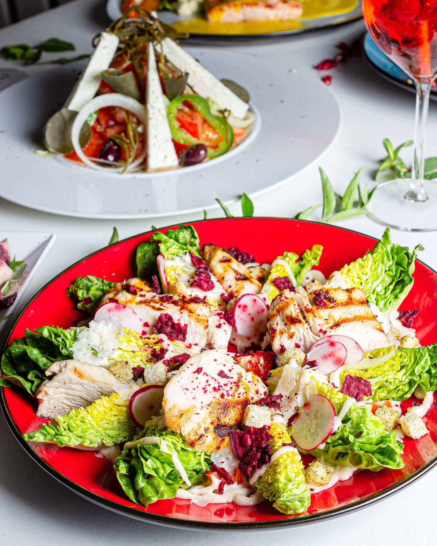 A salad with grilled chicken, radishes, and a red plate.