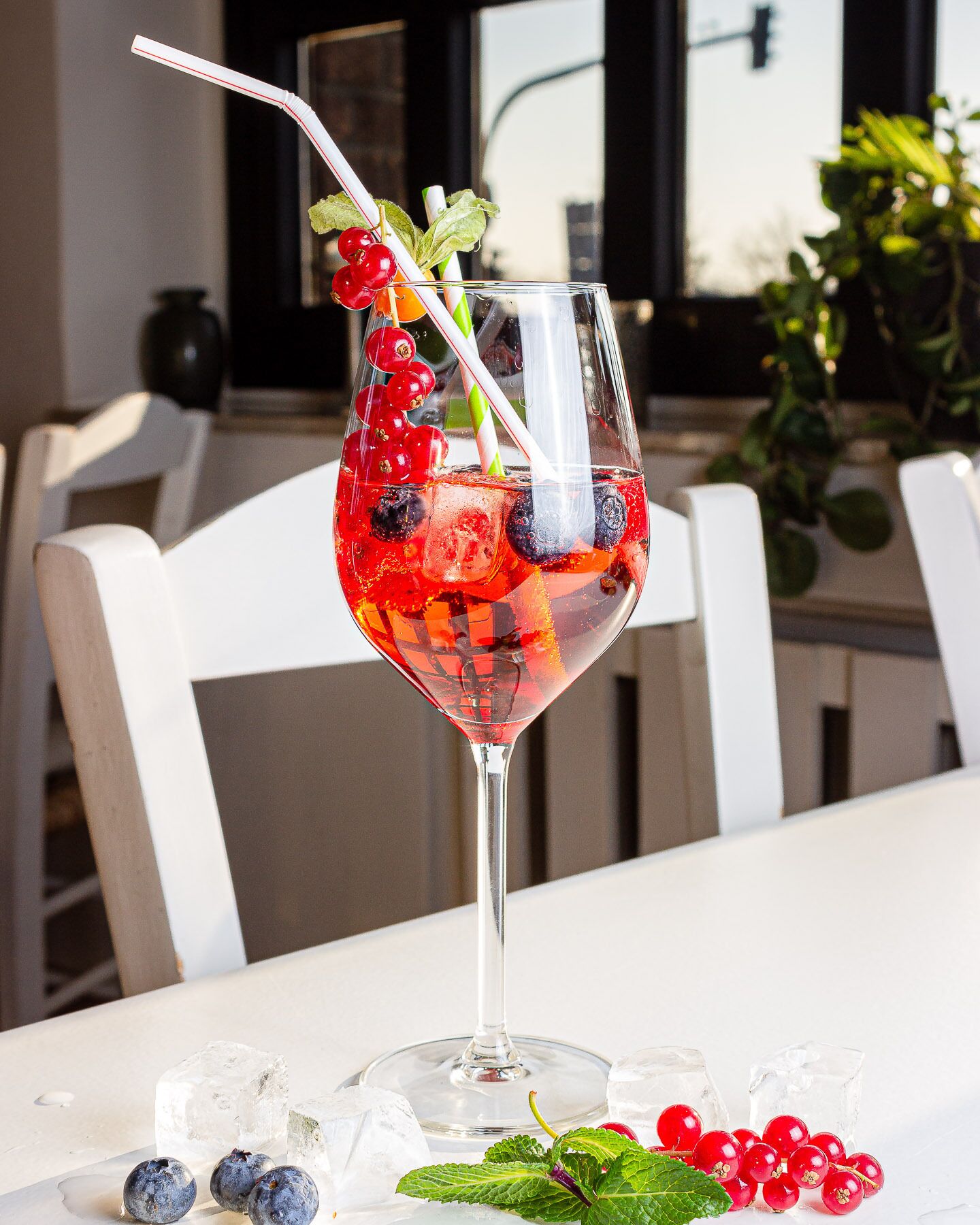 Un vaso de bebida roja con bayas y menta sobre una mesa con cubitos de hielo y más bayas.