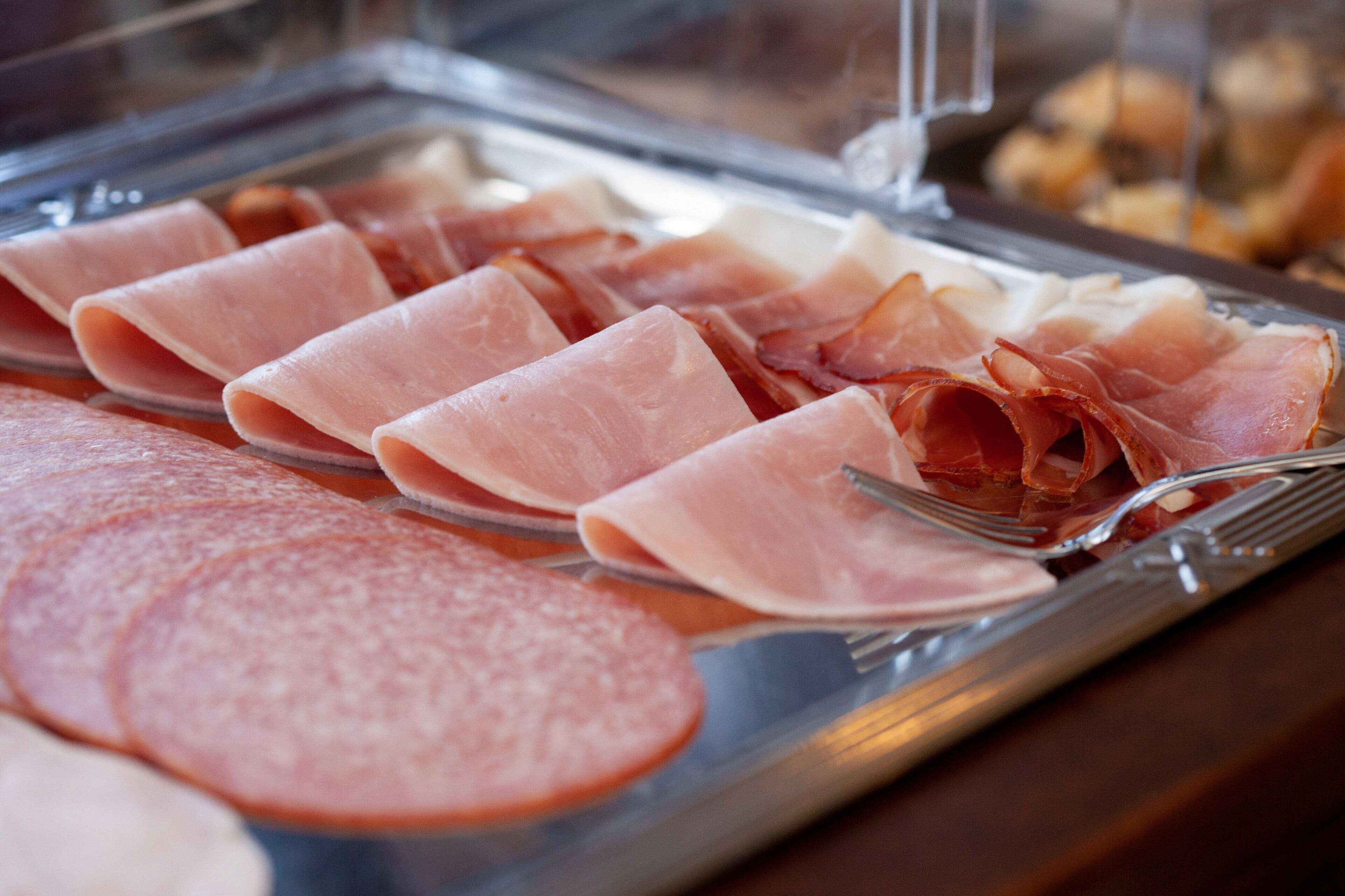 A glass display case with various types of sliced meats, including ham and salami.