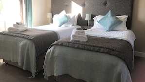 A hotel room with two beds, each with a grey headboard, white linens, and teal pillows. There are folded towels on each bed. - Woodsome Hall Golf Club Cottage on the Course (Huddersfield)
