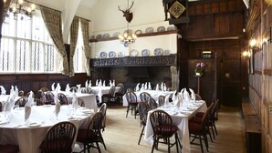 A dining area with multiple tables set for a meal, wooden chairs, a chandelier, and a large fireplace with decorative plates above it. - Woodsome Hall Golf Club Cottage on the Course (Huddersfield)