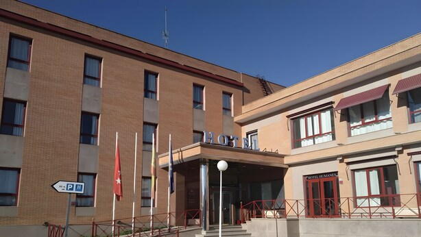 A hotel entrance with a clear sky, a flag, and a sign indicating parking.