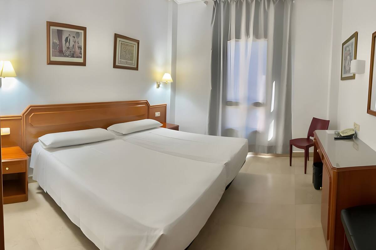 A hotel room with a large bed, bedside tables, a desk with a telephone, and a chair.