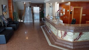 A hotel lobby with a reception desk, seating area, and a staircase leading to an elevator.