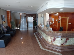 A hotel lobby with a reception desk, seating area, and a staircase leading to an elevator. - Hotel Humanes (Humanes de Madrid)