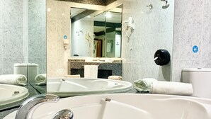 A modern bathroom with a large bathtub, a vanity with a mirror, and a hand dryer.
