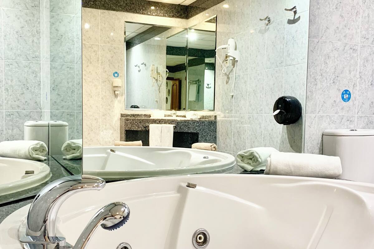 A modern bathroom with a large bathtub, a vanity with a mirror, and a hand dryer.