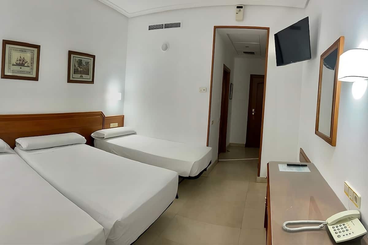 A hotel room with two single beds, a desk with a telephone, and a mirror.